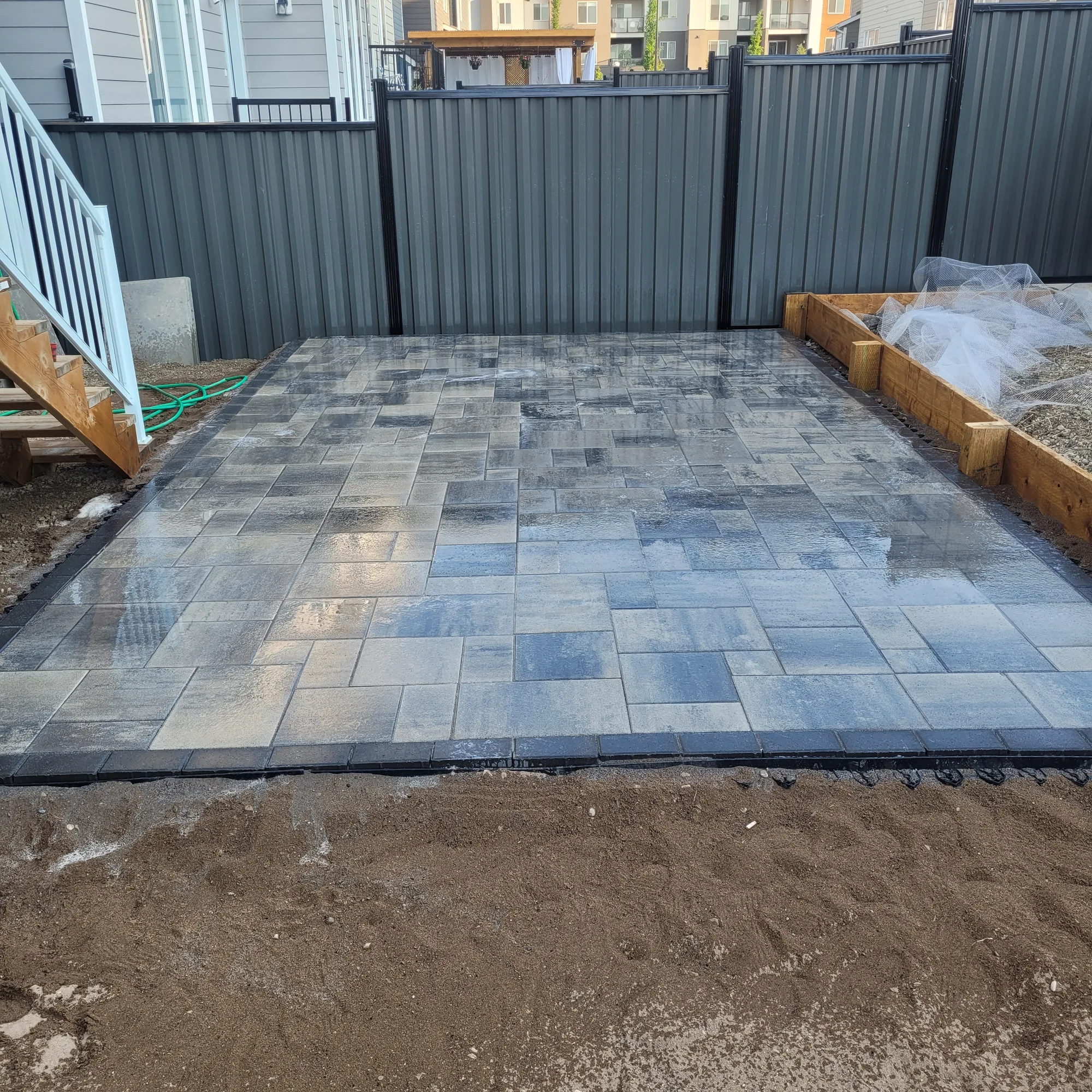 Patterned patio pavers installed beside a backyard fence and raised garden bed in Calgary.