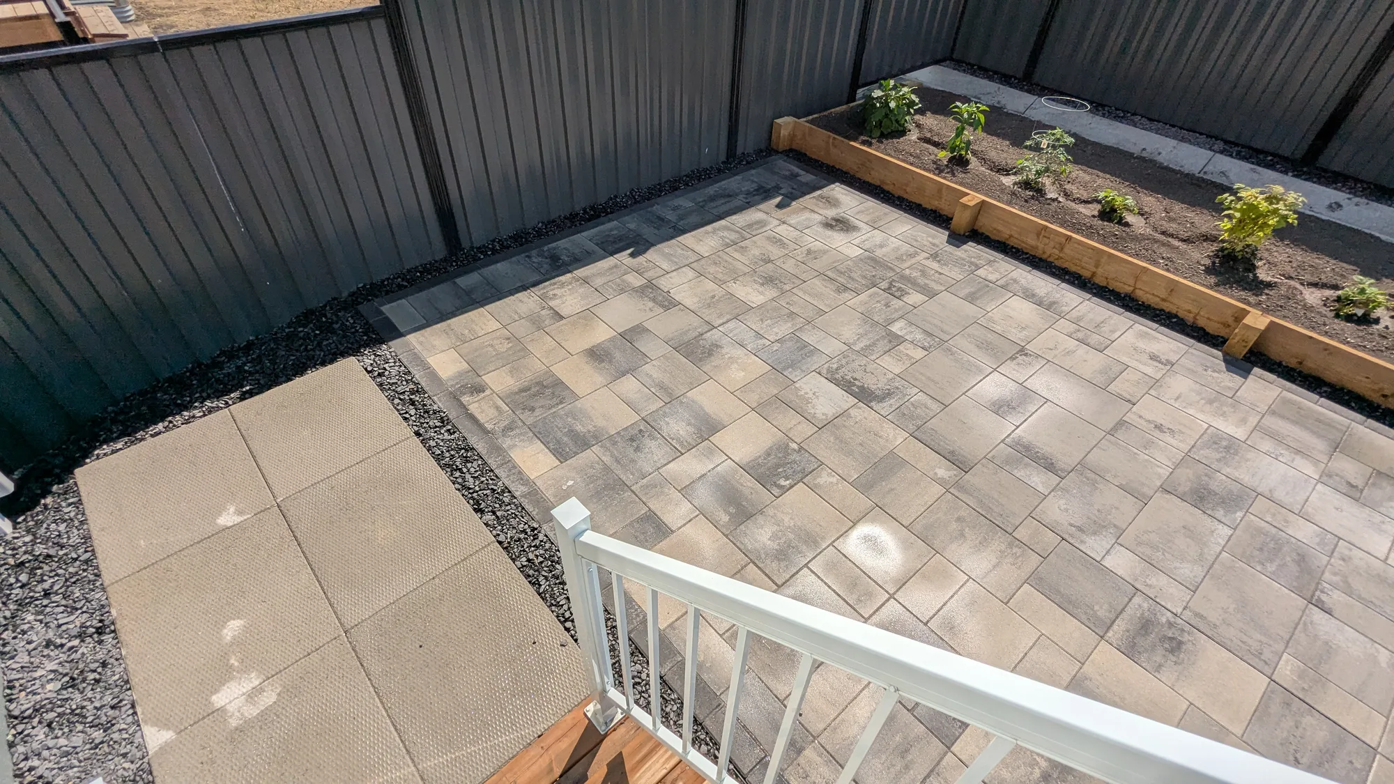 Newly installed patio pavers beside raised garden beds and a privacy fence in a Calgary backyard.