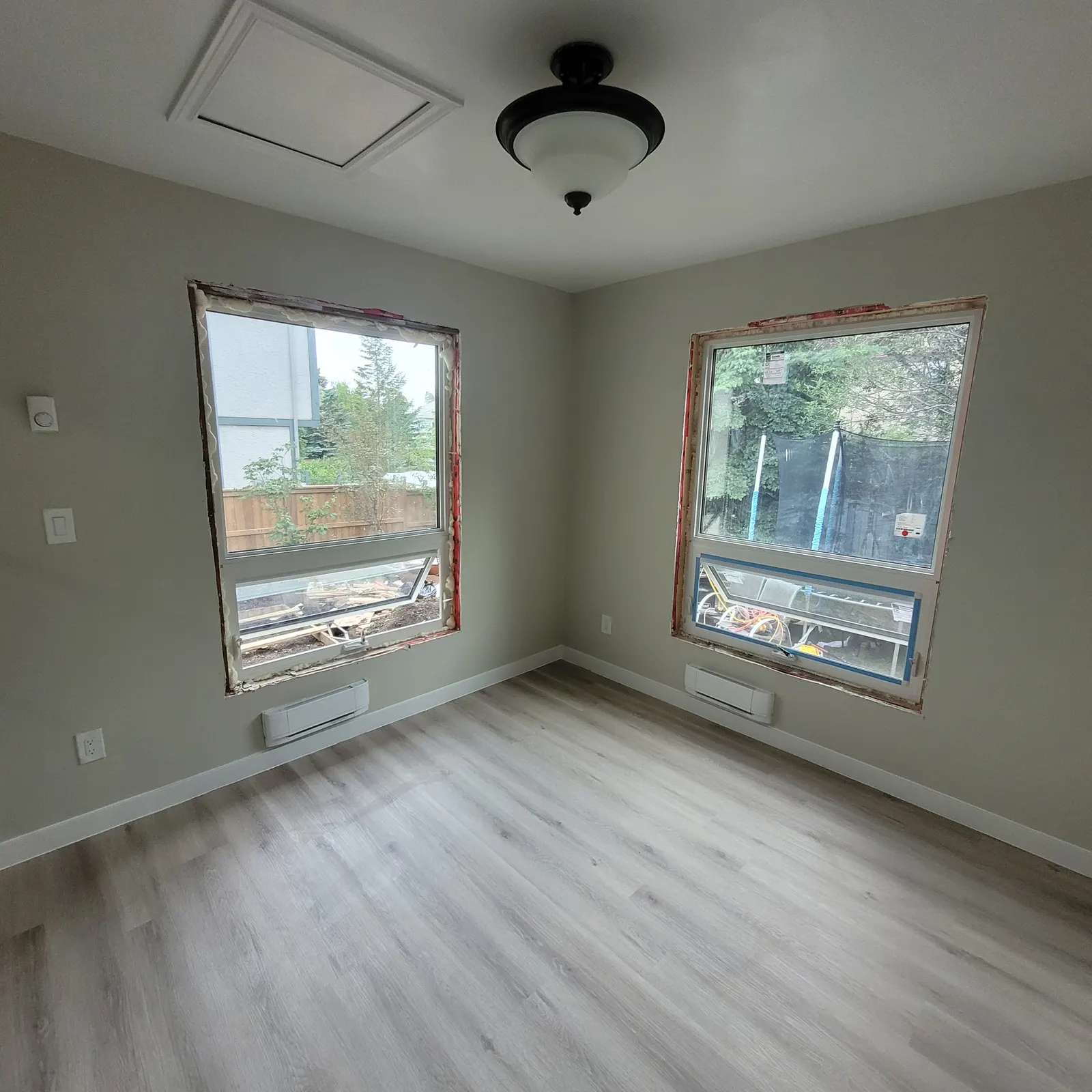 House addition interior with windows awaiting final trim, neutral walls, white baseboards, light wood-look flooring and a ceiling fan.