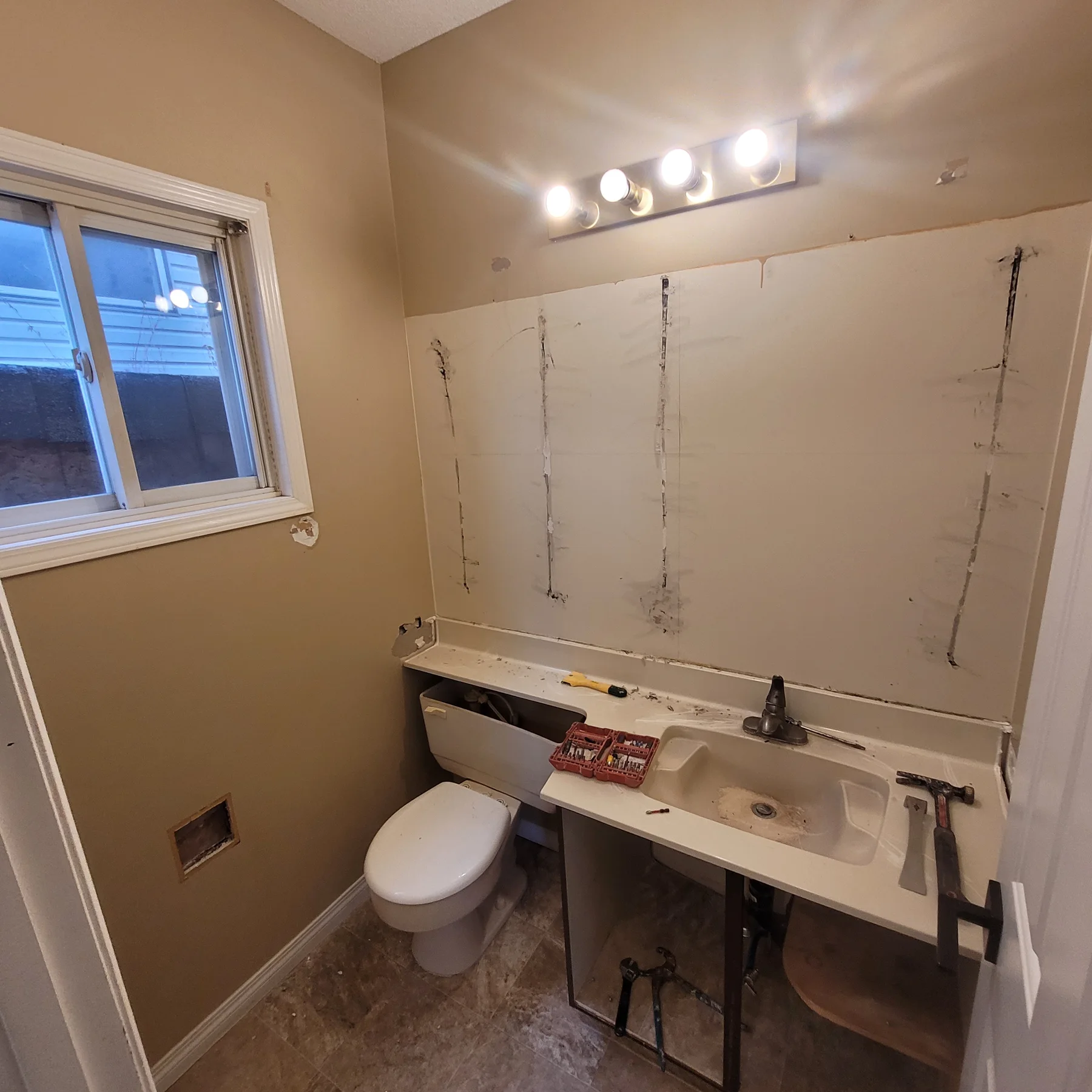Bathroom before renovation with the mirror removed, exposed vanity cabinetry and wall surfaces awaiting repairs.