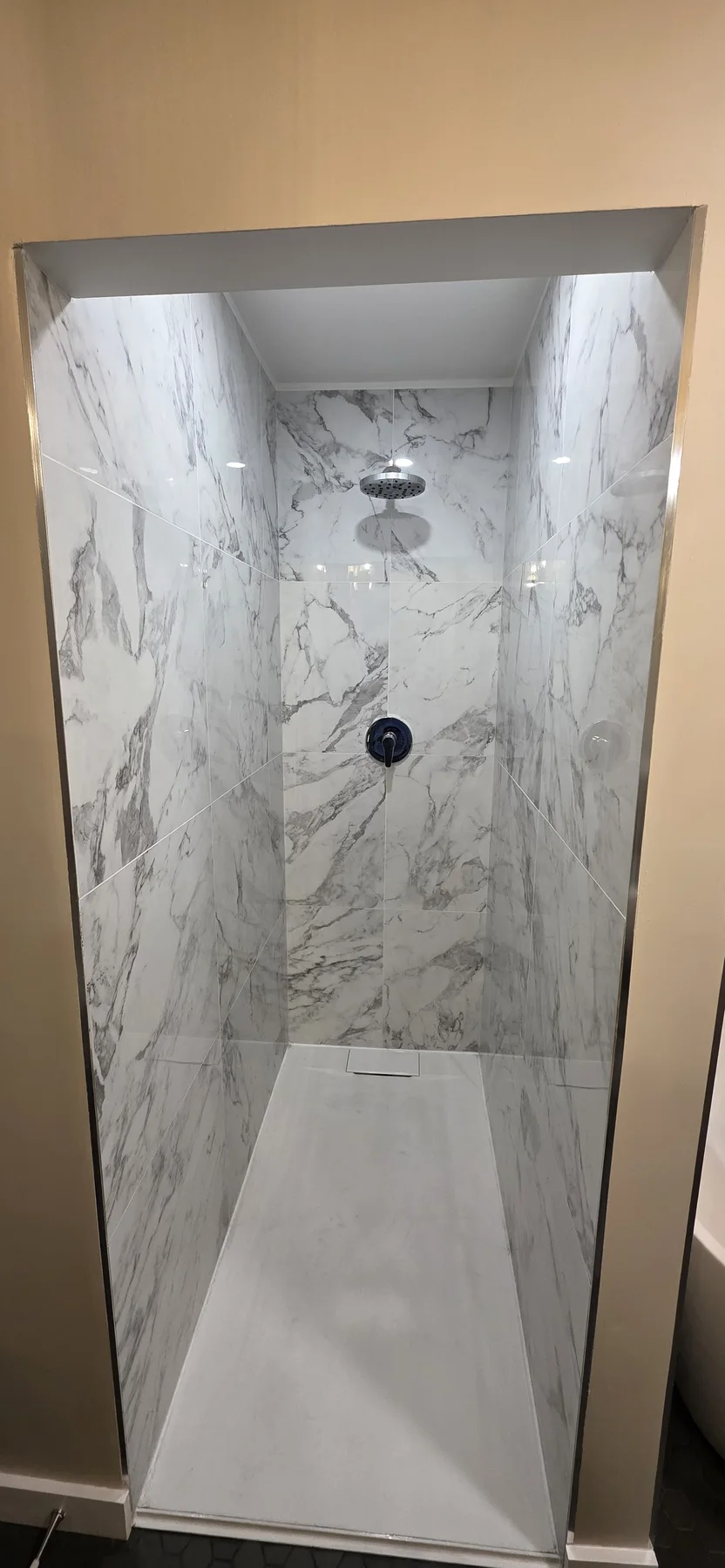 Walk-in shower with white and grey marble-look wall tile, chrome overhead showerhead and white shower base.