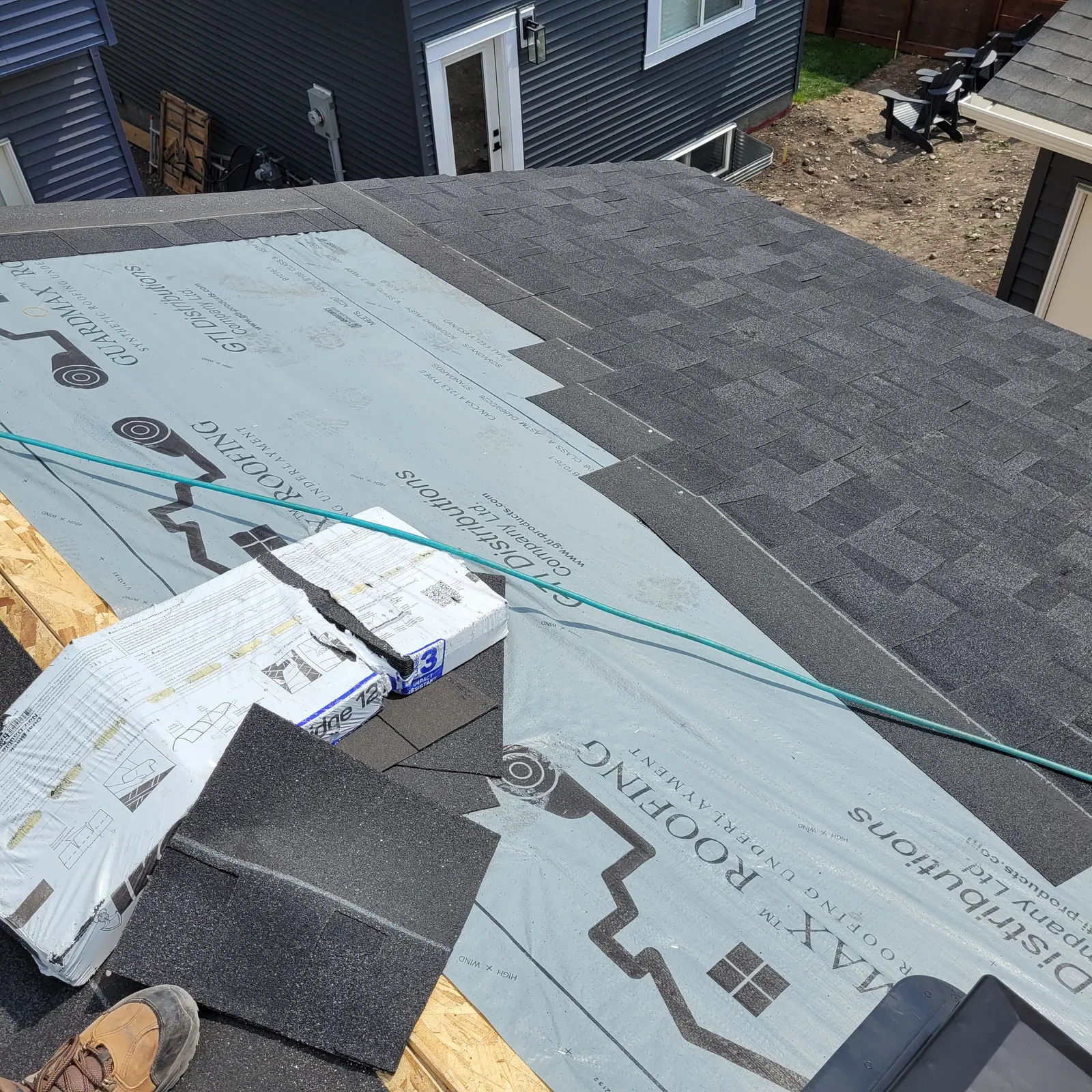 Detached garage roof during construction with partially installed grey asphalt shingles, exposed underlayment and roofing materials.