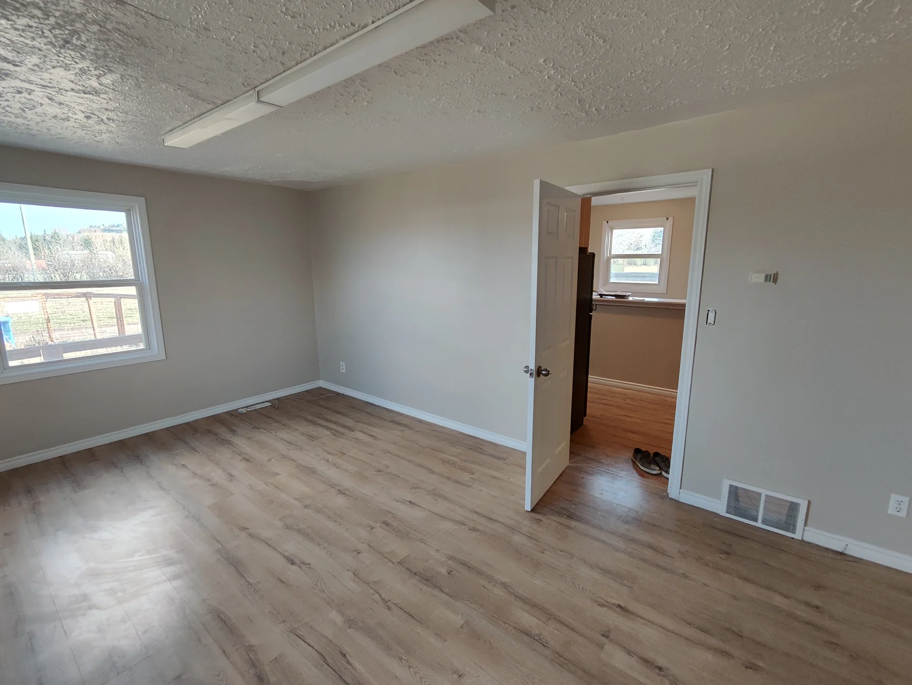 Finished bedroom with neutral walls, wood-look flooring and an open doorway to an adjoining room.