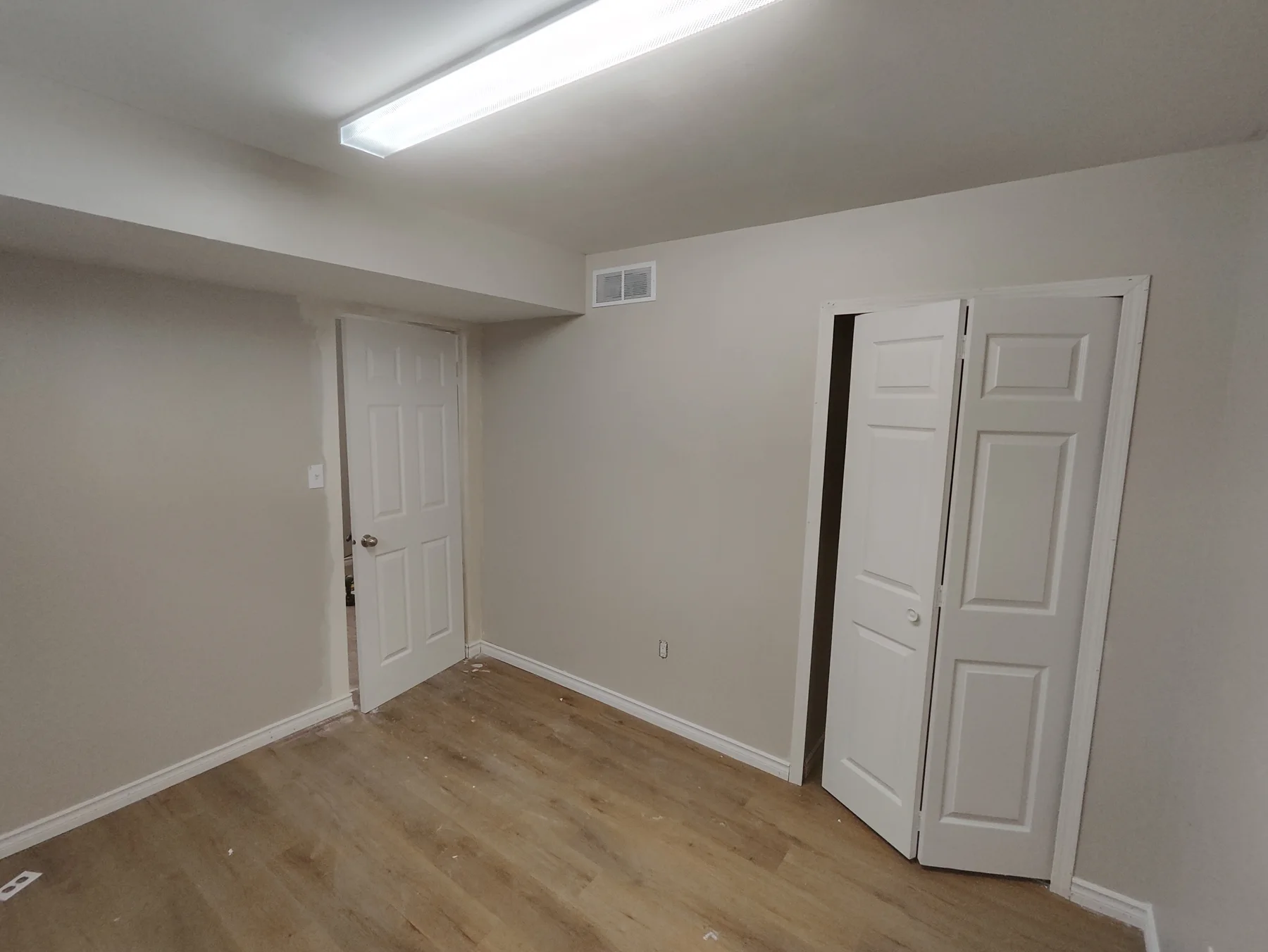 Finished basement room with wood-look flooring, grey walls, white closet doors and a ceiling bulkhead.