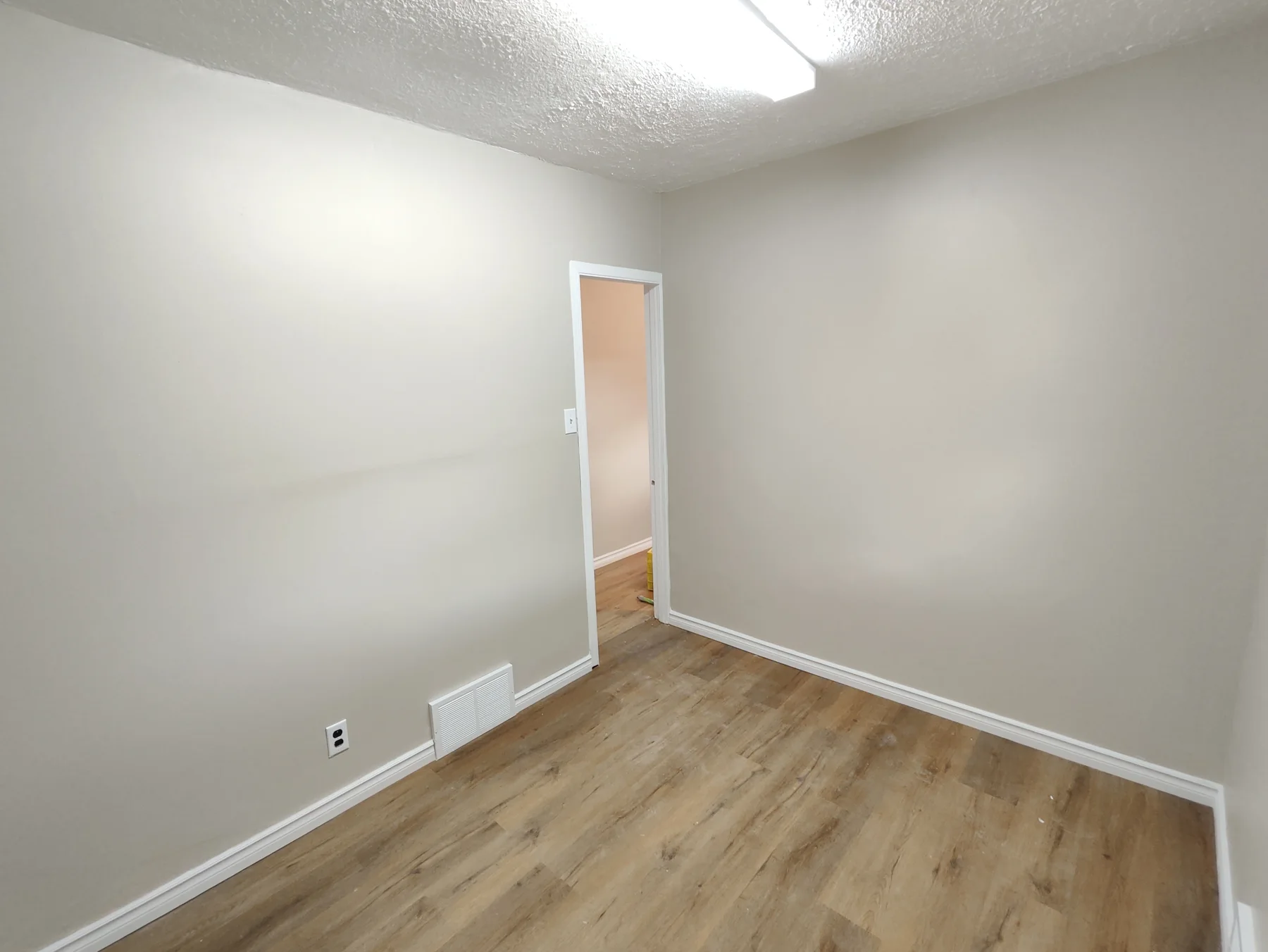 Renovated bedroom with grey walls, white baseboards and wood-look flooring.
