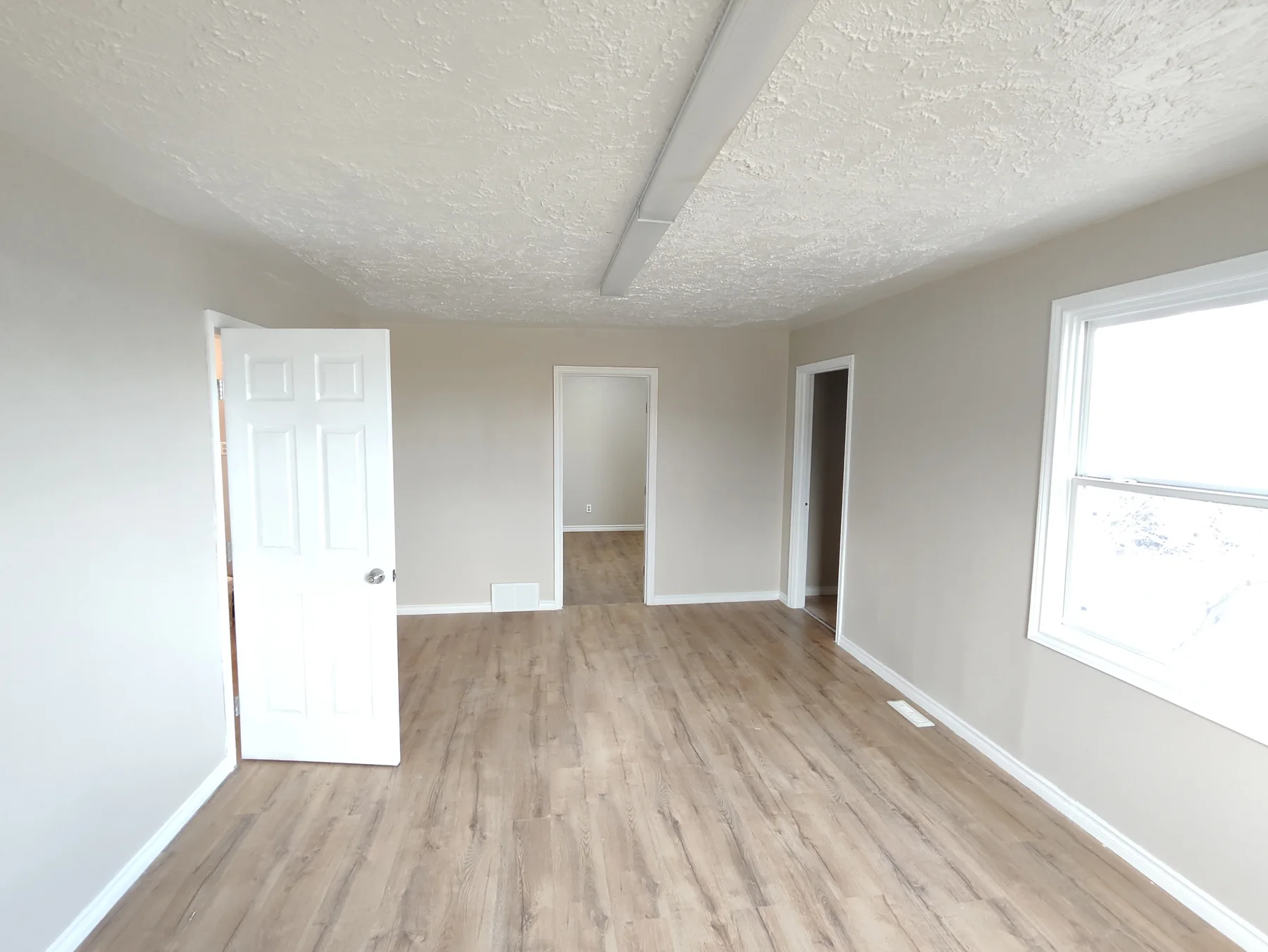 Renovated living space with grey walls, white trim, wood-look flooring and a large window.