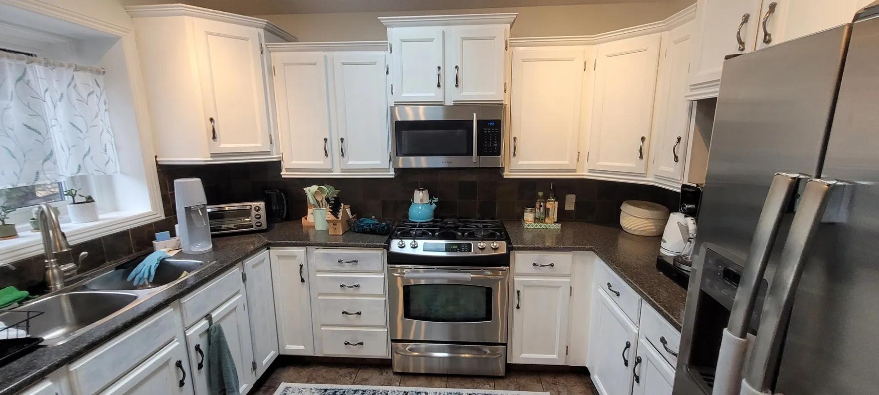 Original Kavan kitchen with white cabinets, dark countertops and backsplash, a window over the sink and stainless steel appliances.