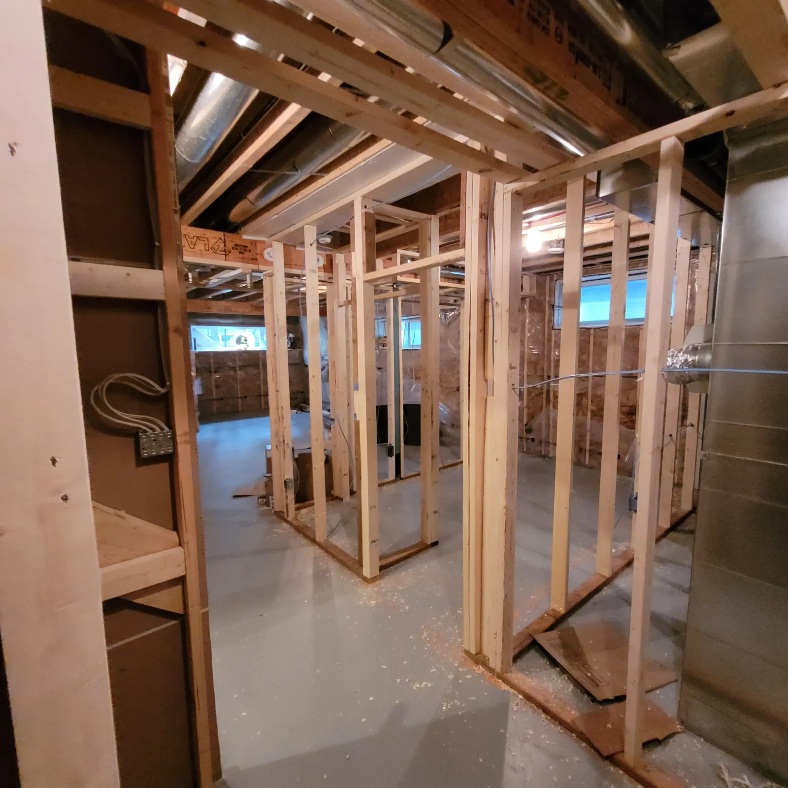 Basement under construction with wood partition framing, framed openings, exposed ceiling joists and services, and a concrete floor.