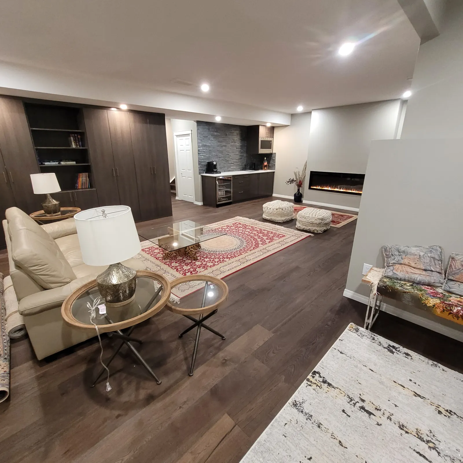 Finished basement living area with seating, a patterned rug, dark built-in cabinets, a wet bar, recessed lights and a linear fireplace.