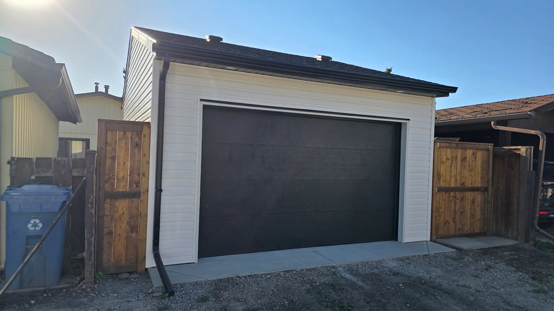 Completed single detached garage with white siding, dark roof trim, a dark overhead door and a concrete apron.