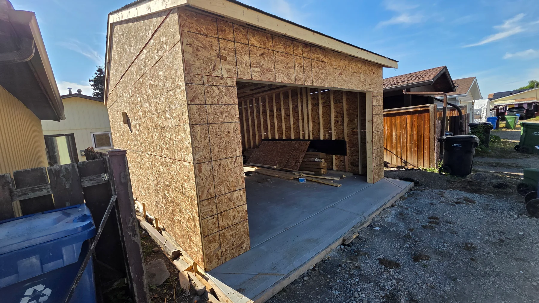 Single detached garage under construction with wood sheathing, exposed framing at the overhead-door opening and a concrete slab.