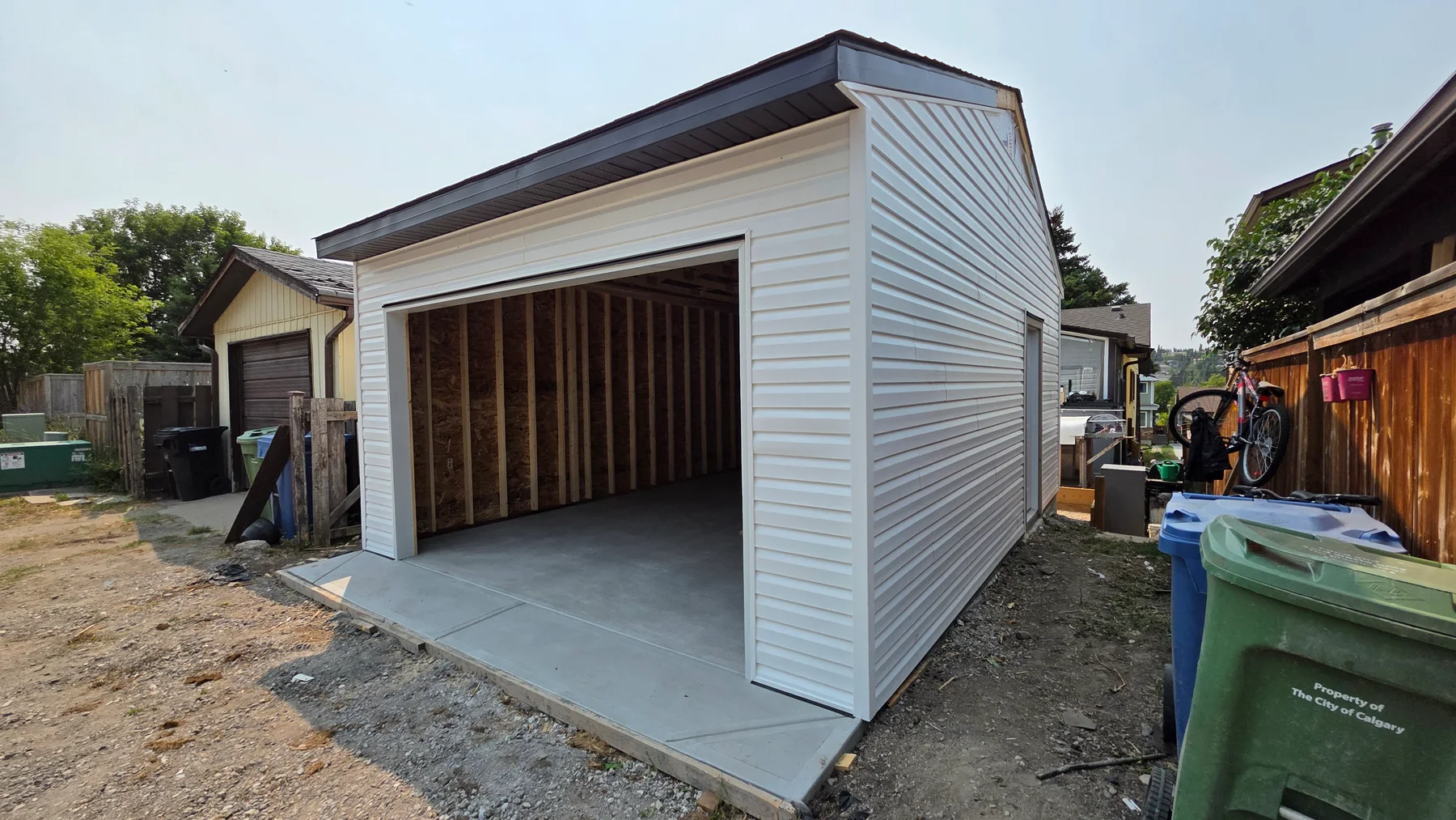 Single detached garage with white horizontal siding and dark roof trim, shown before the overhead garage door was installed.