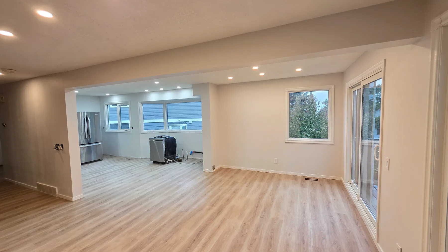 Renovated living area with a wide opening beneath an enclosed beam, light wood-look flooring, recessed lighting, a window and sliding patio door.