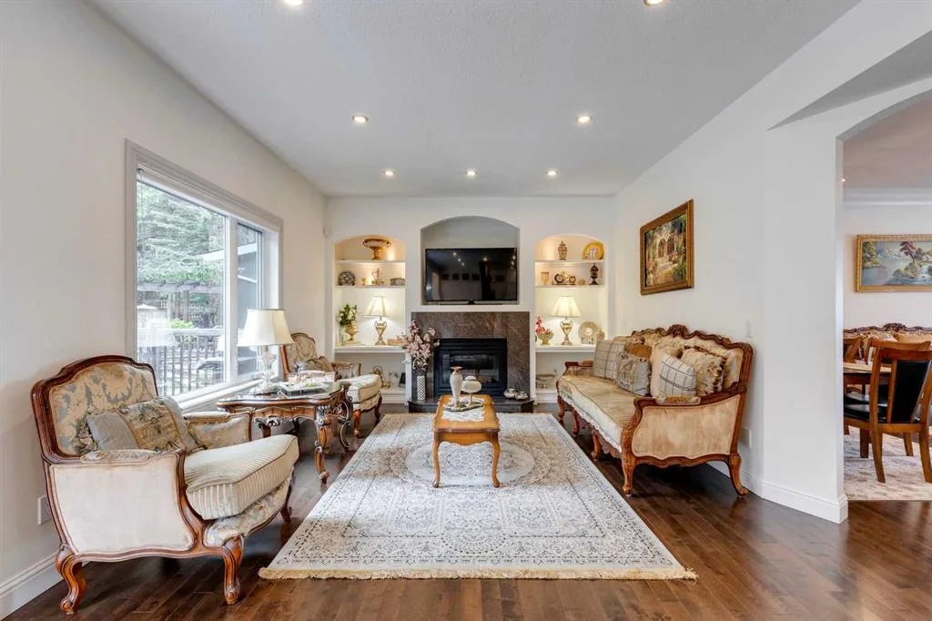 Original living room with a fireplace, built-in shelves, traditional furniture and a smaller opening to the dining room on the right.