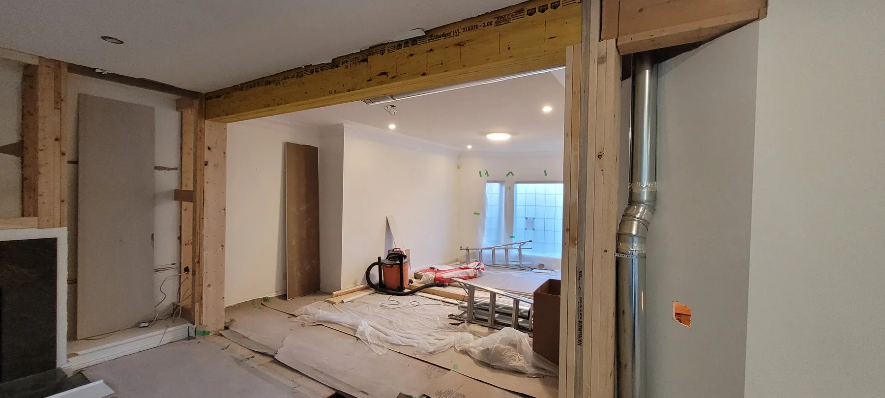 Wide interior opening during load-bearing wall removal, with an exposed wood beam, wall framing and protected floors.
