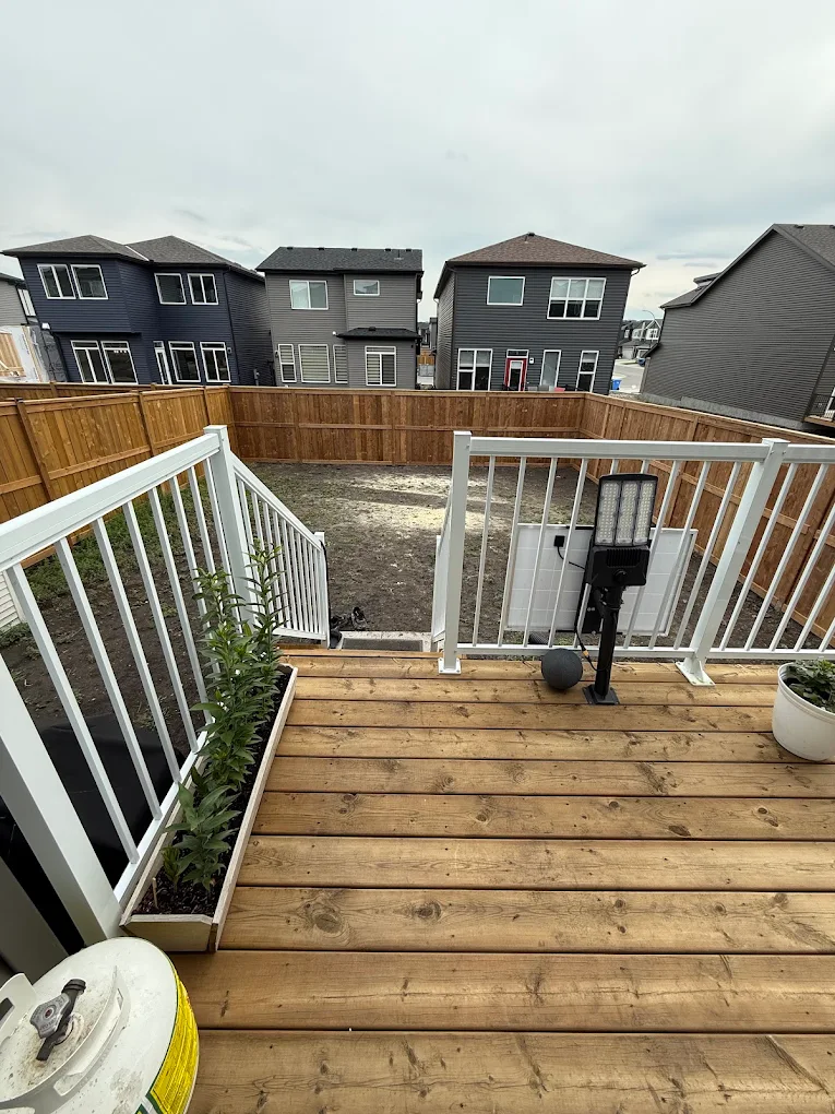 Completed wood deck with white railings leading into a fenced Calgary backyard.