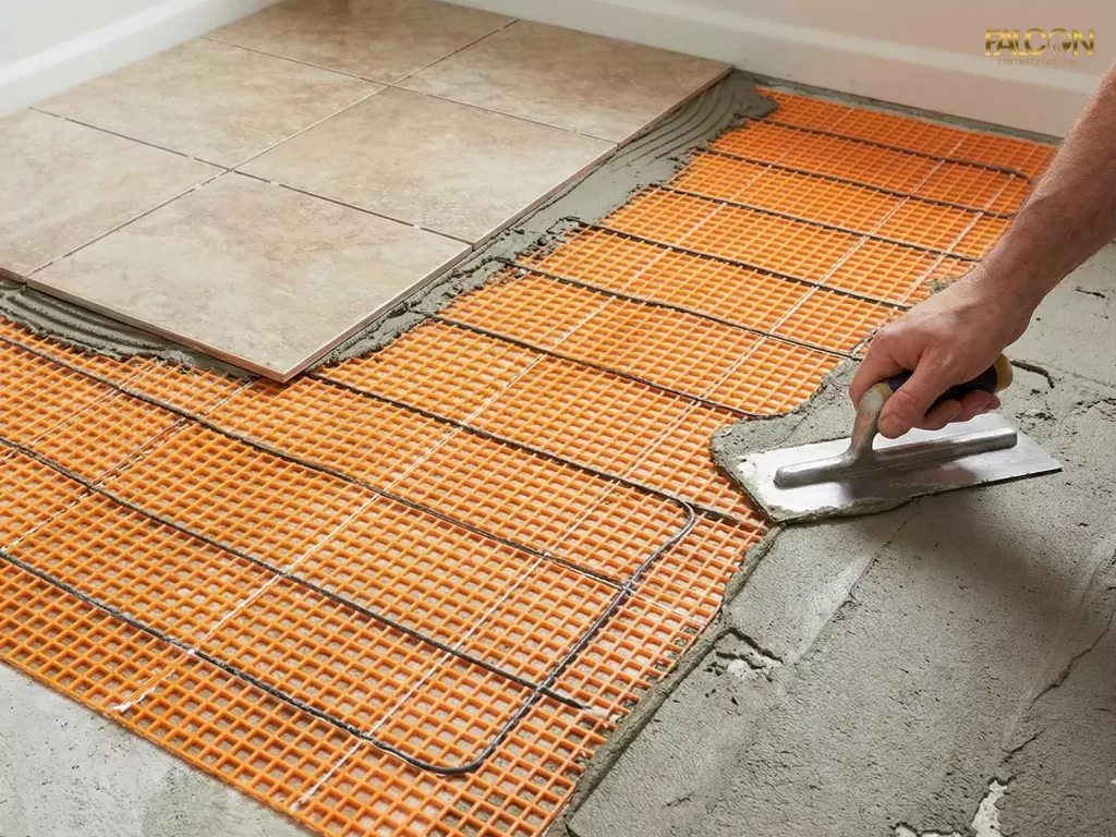 A construction photo showing a radiant electric heating mat being installed directly onto a concrete subfloor before being covered by bathroom tiles.