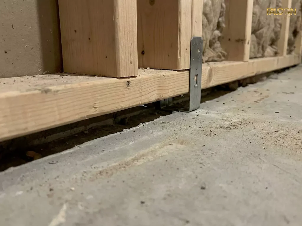 Close-up of a floating wall in a Calgary basement showing the required gap between the bottom framing plate and the concrete floor slab, secured with a metal bracket.