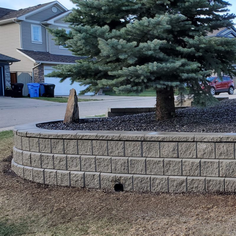 Construction site featuring multiple structures with new blue vinyl siding, and a wooden retaining wall being built in the foreground with scattered lumber and a silver ladder.
