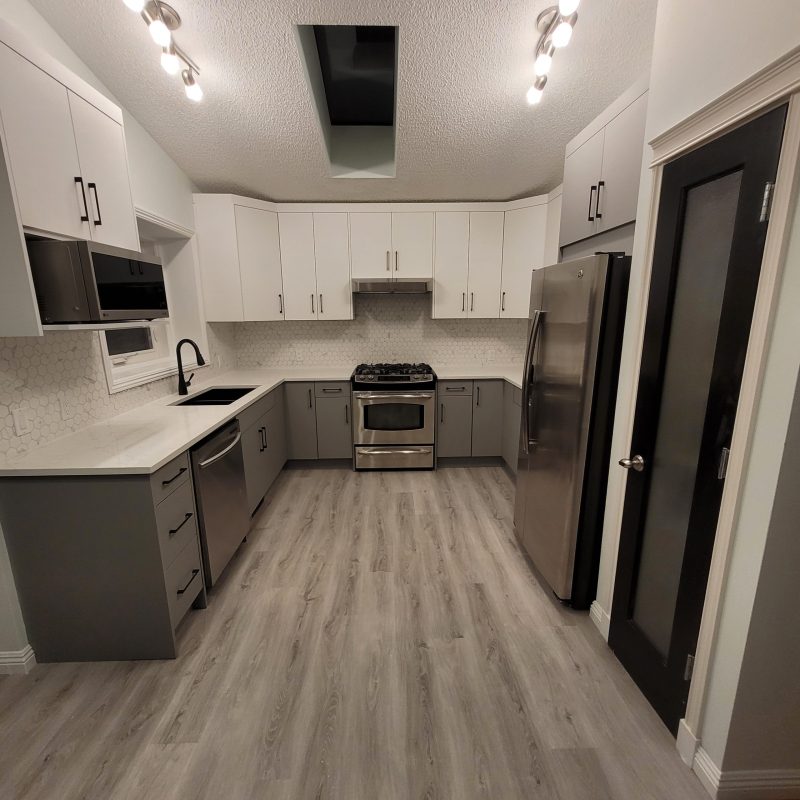 Interior view of a renovated kitchen featuring two-tone cabinetry with white uppers and grey lowers, a geometric hexagon tile backsplash, stainless steel appliances, and a skylight.